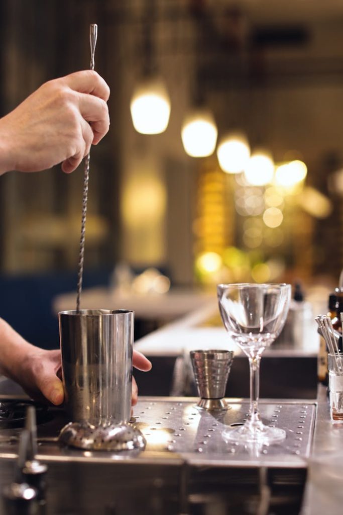 Close-up of bartender stirring cocktail with bar tools in a lively bar setting.