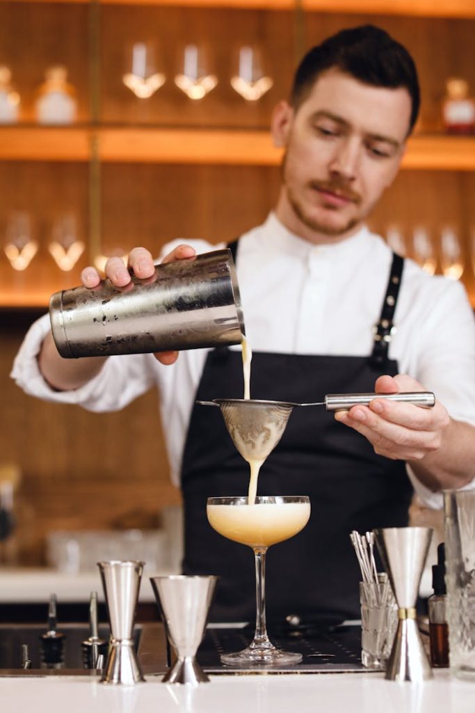 Bartender pouring a fresh cocktail using a shaker and strainer at a modern bar.